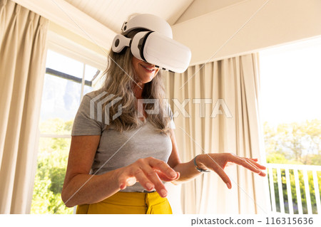 Using VR headset, mature woman exploring virtual reality at home Using VR headset, mature woman exploring virtual reality at home 116315636