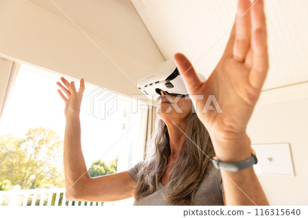 Using VR headset, mature woman exploring virtual reality at home Using VR headset, mature woman exploring virtual reality at home 116315640
