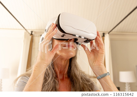Using VR headset, mature woman exploring virtual reality at home 116315642