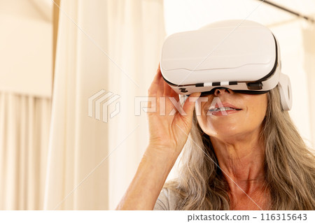 Using VR headset, mature woman exploring virtual reality at home 116315643