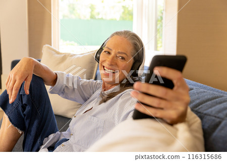 Listening to music with headphones, mature woman smiling and holding smartphone 116315686
