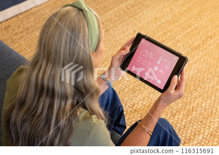 Using tablet, mature woman controlling smart home devices in living room Using tablet, mature woman controlling smart home devices in living room 116315691