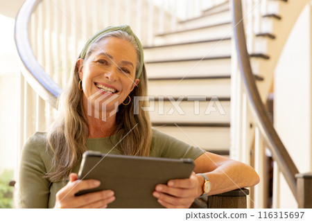 Smiling woman using tablet while sitting on staircase at home 116315697