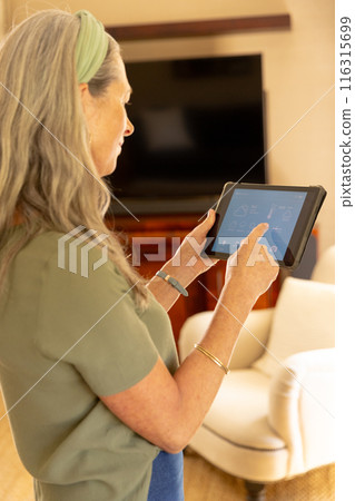 Using tablet, mature woman managing smart home devices in living room Using tablet, mature woman managing smart home devices in living room 116315699