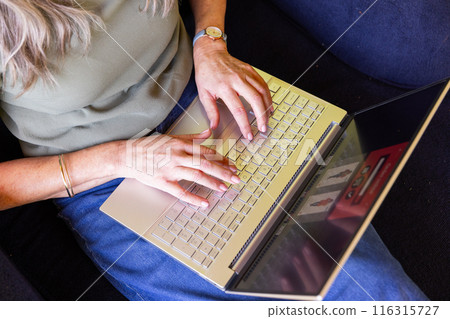 Typing on laptop, mature woman working from home on couch in casual attire 116315727