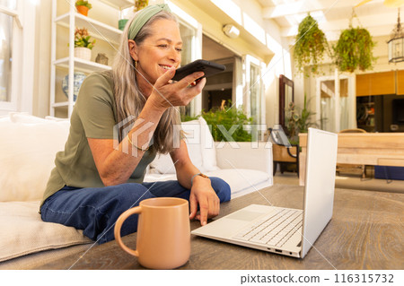 Smiling mature woman using smartphone and laptop while working from home on patio 116315732