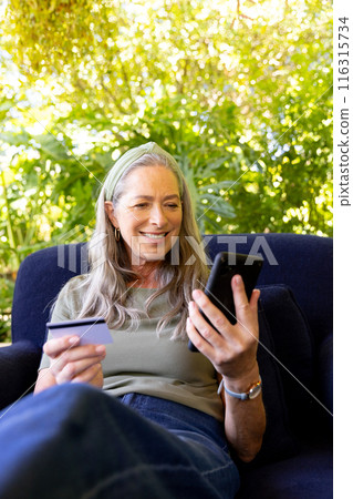 Using smartphone and holding credit card, mature woman shopping online from home, copy space 116315734
