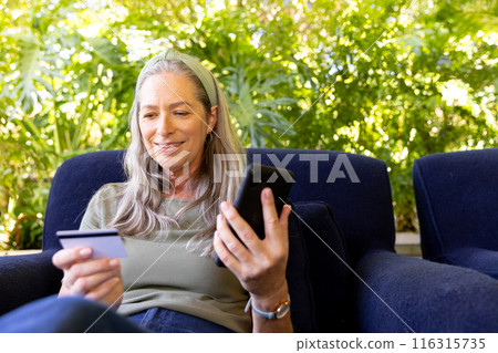 Shopping online, mature woman holding smartphone and credit card, sitting on couch Shopping online, mature woman holding smartphone and credit card, sitting on couch 116315735