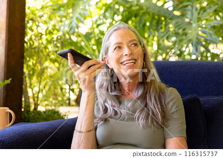 Talking on smartphone, mature woman sitting on couch and smiling outdoors 116315737