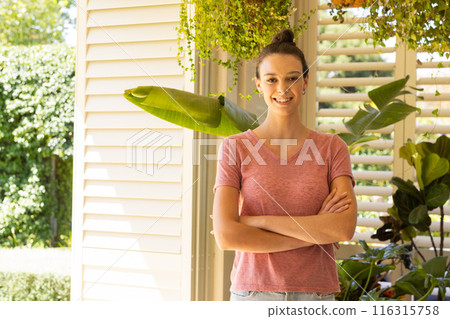 Smiling young woman standing with arms crossed in bright home garden, copy space Smiling young woman standing with arms crossed in bright home garden, copy space 116315758
