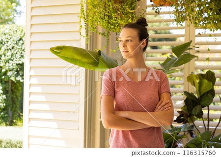 Standing with arms crossed, young woman looking outside in bright home 116315760