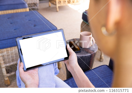 Holding tablet, woman sitting on patio with coffee mug nearby, copy space 116315771