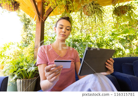 Using tablet and holding credit card, woman shopping online in garden Using tablet and holding credit card, woman shopping online in garden 116315781