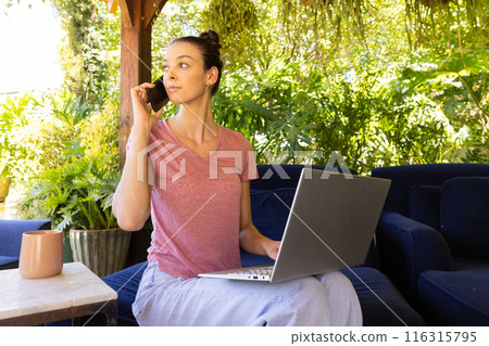 Working from home, woman using laptop and talking on smartphone outdoors 116315795