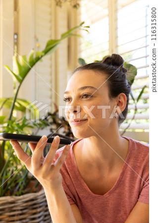 Using smartphone, young woman recording voice message in bright home setting 116315800