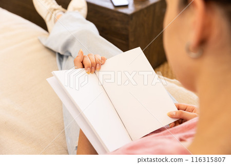 Reading blank notebook, woman relaxing on couch at home, copy space Reading blank notebook, woman relaxing on couch at home, copy space 116315807