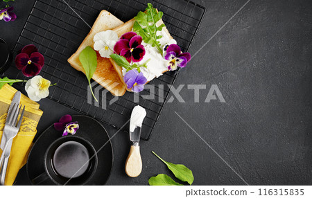 brioche toast with cream cheese and pansy flowers on a plate. Gourmet breakfast. Selective focus, black background, copy space 116315835