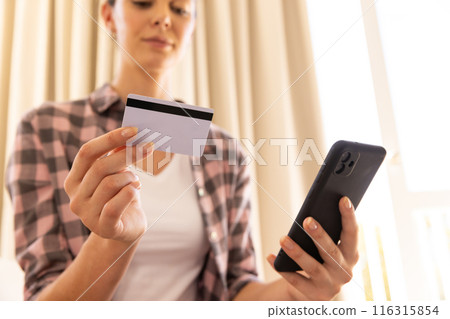 Holding credit card and smartphone, woman making online payment at home 116315854