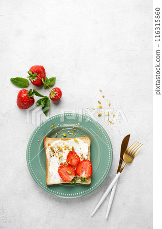 Sandwich with strawberries, soft cheese, pistachios on green plate on white background. Top view. copy space 116315860