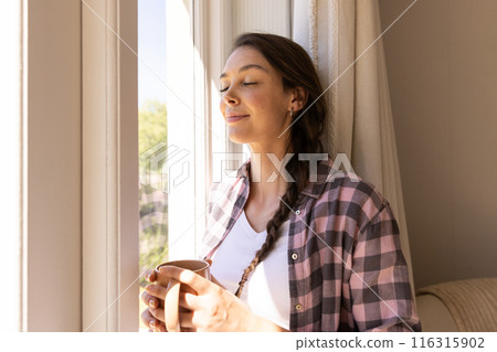 Relaxing by window, woman holding coffee cup and enjoying sunlight at home Relaxing by window, woman holding coffee cup and enjoying sunlight at home 116315902