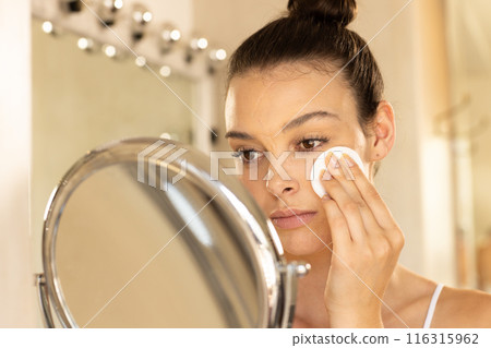Applying makeup, young woman using cotton pad in front of mirror 116315962