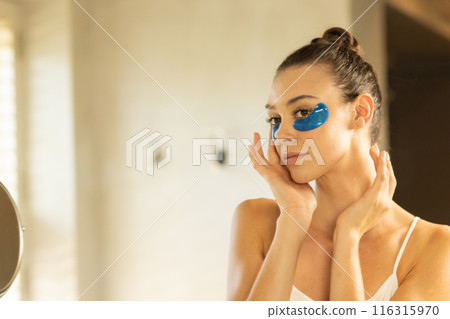 Applying under-eye patches, woman focusing on skincare routine in bathroom, copy space Applying under-eye patches, woman focusing on skincare routine in bathroom, copy space 116315970