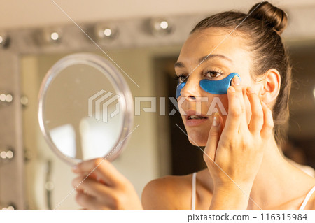 Applying under-eye patches, woman looking in mirror for skincare routine 116315984
