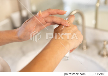 Applying lotion on hands, woman taking care of skin in bathroom 116315985