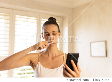 Brushing teeth, woman using smartphone and looking at screen in bathroom Brushing teeth, woman using smartphone and looking at screen in bathroom 116315986
