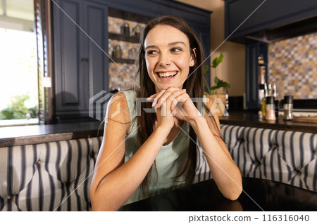 Smiling woman sitting at kitchen table, enjoying her time at home Smiling woman sitting at kitchen table, enjoying her time at home 116316040