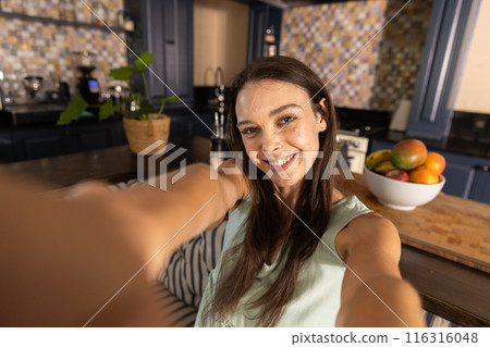 Taking selfie, woman smiling in kitchen with fruit bowl on counter Taking selfie, woman smiling in kitchen with fruit bowl on counter 116316048