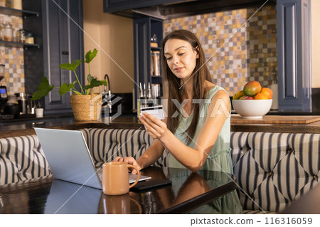 Shopping online, woman using laptop and holding credit card in kitchen 116316059