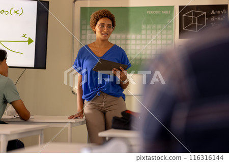In high school, teacher holding tablet and explaining lesson to students in classroom 116316144