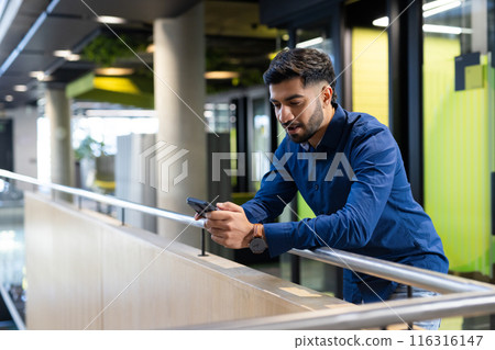 Using smartphone, man leaning on railing in modern office building, copy space 116316147