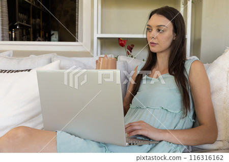 Using laptop and drinking coffee, woman working from home on couch Using laptop and drinking coffee, woman working from home on couch 116316162