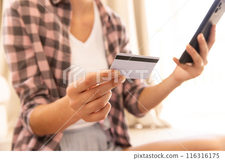 Holding credit card and smartphone, woman making online purchase at home 116316175