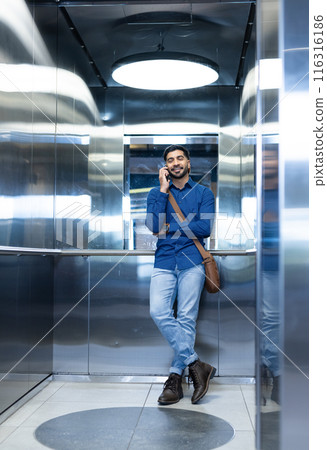 Talking on smartphone, man in business casual attire standing in elevator 116316186
