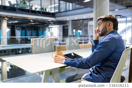 Talking on smartphone, man holding coffee cup and sitting in modern office, copy space 116316211