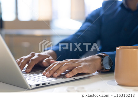 Typing on laptop, man working in office with coffee mug on desk 116316218