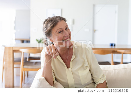 Smiling woman on video call on couch and pointing finger, enjoying vacation time Smiling woman on video call on couch and pointing finger, enjoying vacation time 116316238