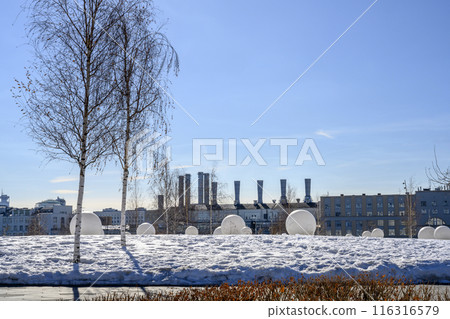Snowy field with white balls and a birch tree on the background of hydroelectric power plant pipes 116316579