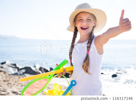 Child in hat on beach shows thumb up 116317146