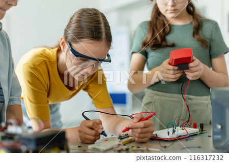 School girls working on circuit board of small robot, building robotic car in after-school robotics club. Children learning robotics in Elementary school. Girls in science. 116317232