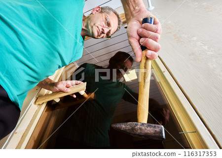 Securing jamb to door frame, nailing wood piece together with hammer. 116317353
