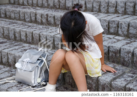 An elementary school student with a disaster prevention backpack and feeling unwell. Sitting on the stairs. An elementary school student with a disaster prevention backpack and feeling unwell. Sitting on the stairs. 116318161