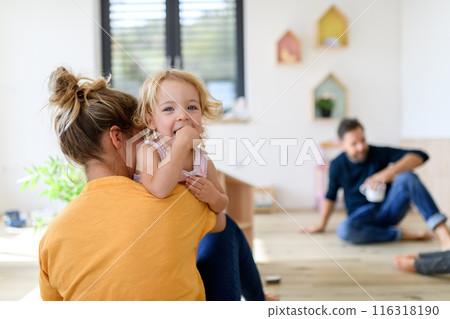 Mom putting clothes on small girl, who trying to run off. Young nuclear family having fun at home, spending weekend day indoors. 116318190