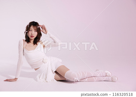 A Korean woman in her 20s who poses on the floor wearing a white ballet core look with a light pink background 116320518