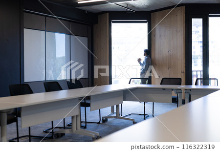 Businessman standing by window in modern office, holding baby and working, copy space 116322319