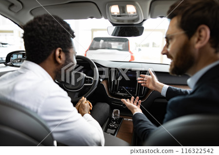 Caucasian car dealer discusses vehicle features with African American buyer 116322542