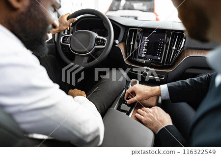 Caucasian car dealer showing features inside vehicle to African American buyer 116322549